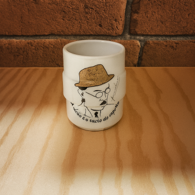 Caneca branca com ilustração e texto numa mesa de madeira e fundo de tijolos