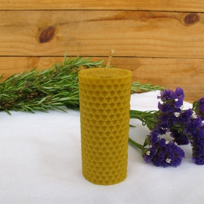 Vela cilíndrica amarela texturizada com flores e ramos verdes ao fundo