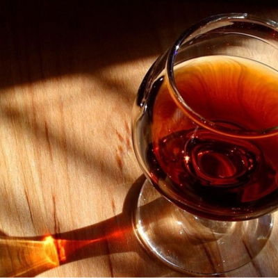 Copo redondo de vidro com líquido castanho sobre madeira clara