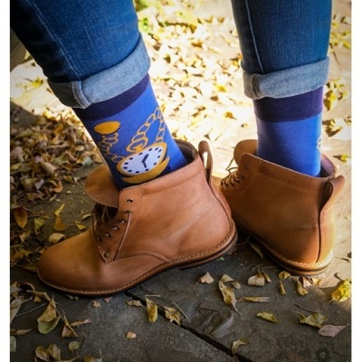 Pessoas com meias azuis com padrão de relógios e botas castanhas de couro em piso de pedra com folhas secas