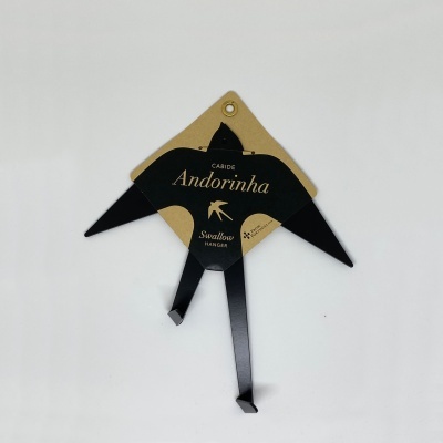 Cabide metálico preto em forma de andorinha com embalagem em cartão castanho.
