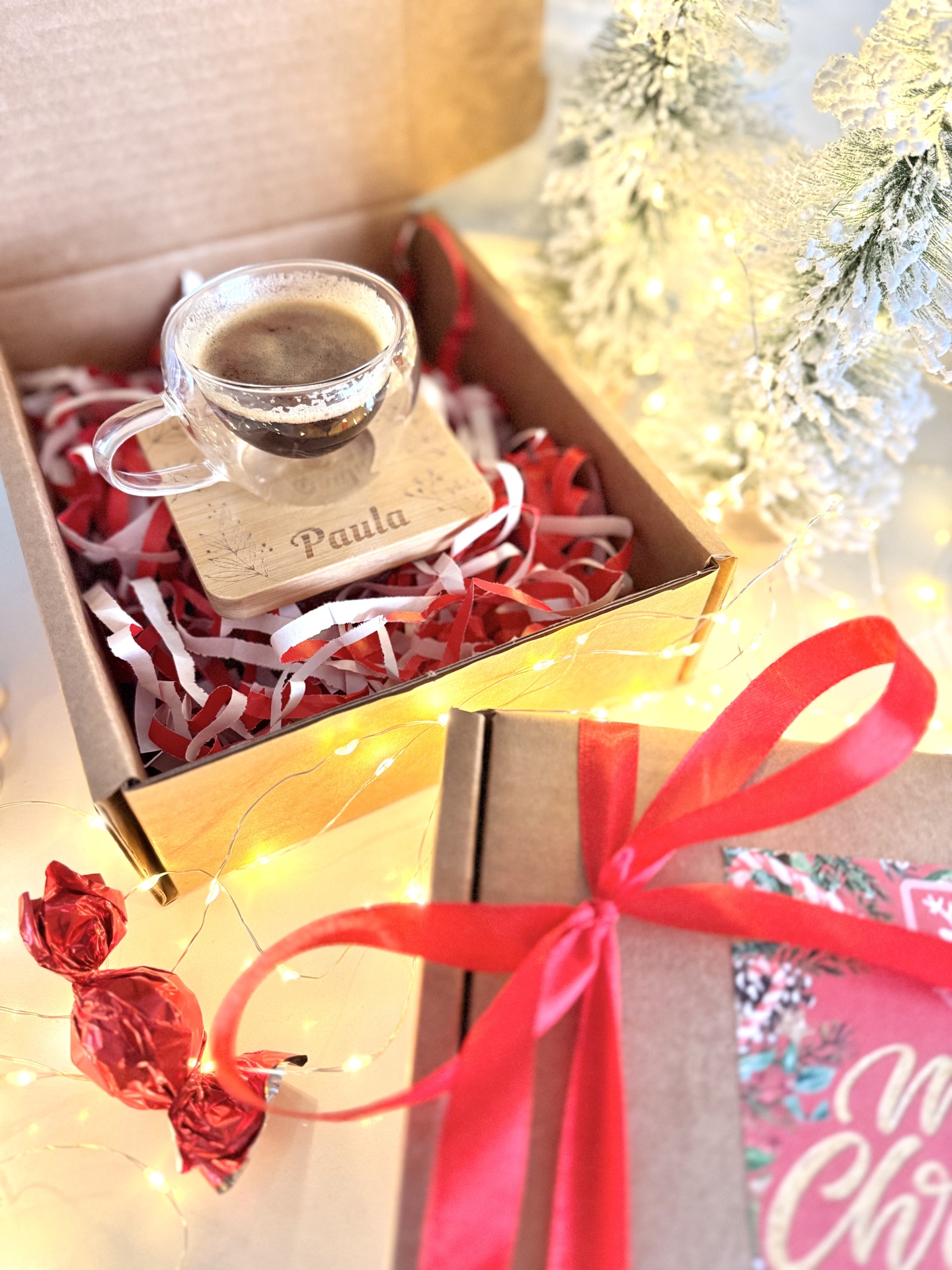 Box Chávena de Café Caixa de oferta com chávena de vidro e suporte de madeira com o nome Paula, doce envolto em papel vermelho, árvores de Natal naturais com neve e luzes