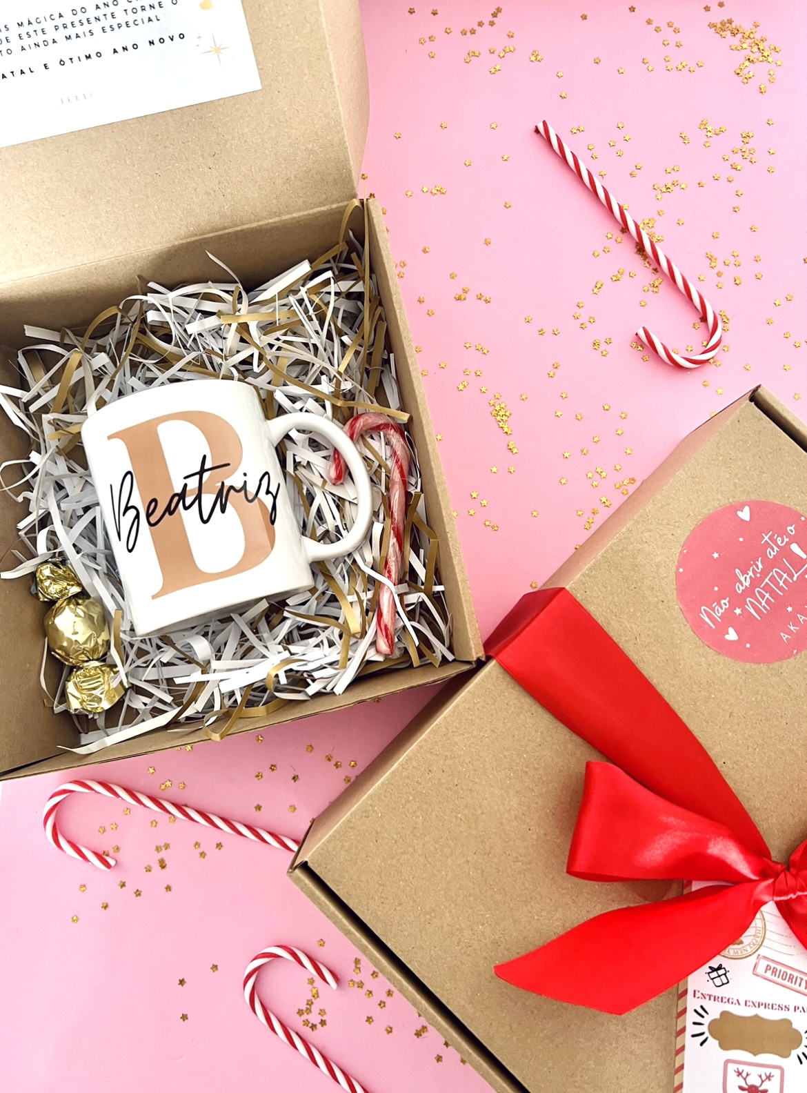 Box Caneca Inicial Conjunto de caneca personalizada com nome Beatriz, bombons e bastões de açúcar em caixa de cartão com fundo rosa e confetis dourados.