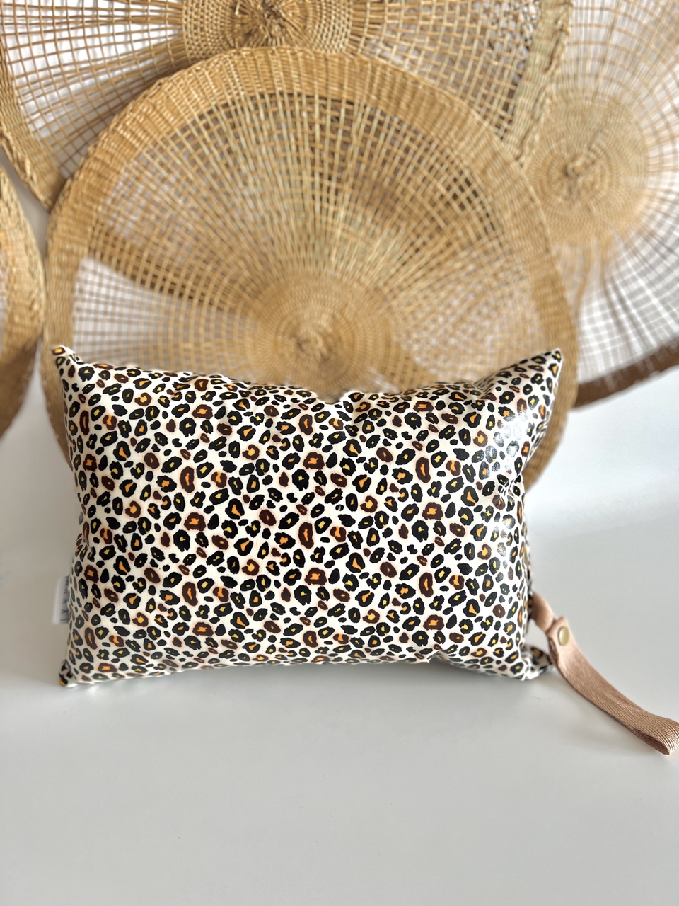 Almofada Leopardo Necessaire com padrão animal print em superfície branca e redes de palha ao fundo
