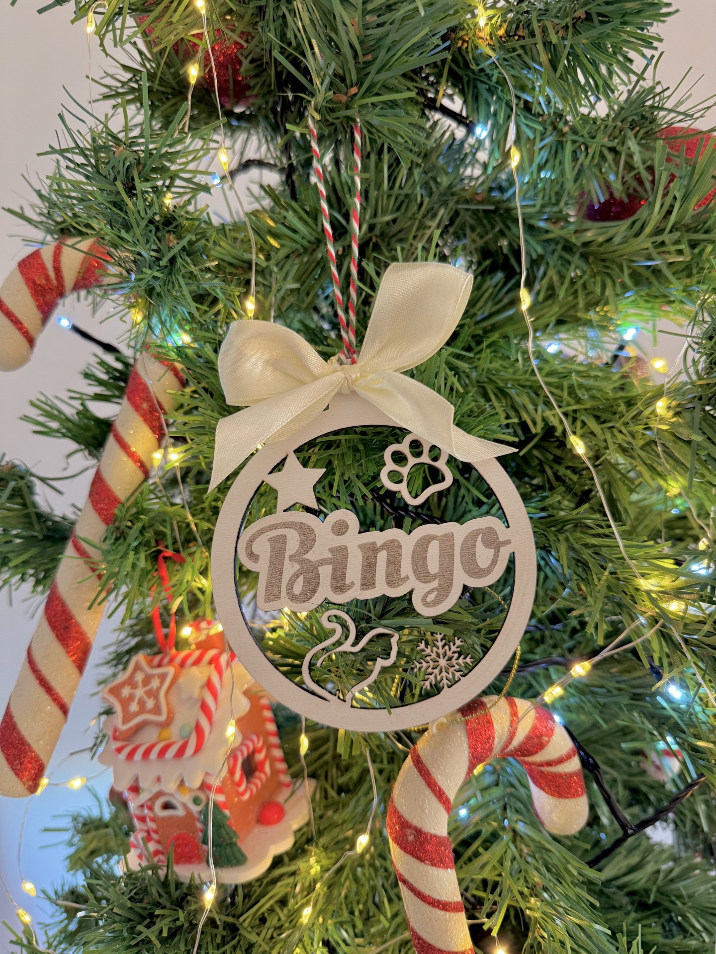 Bola de Natal com nome Ornamento de Natal de madeira com o nome Bingo pendurado numa árvore com luzes e decorações