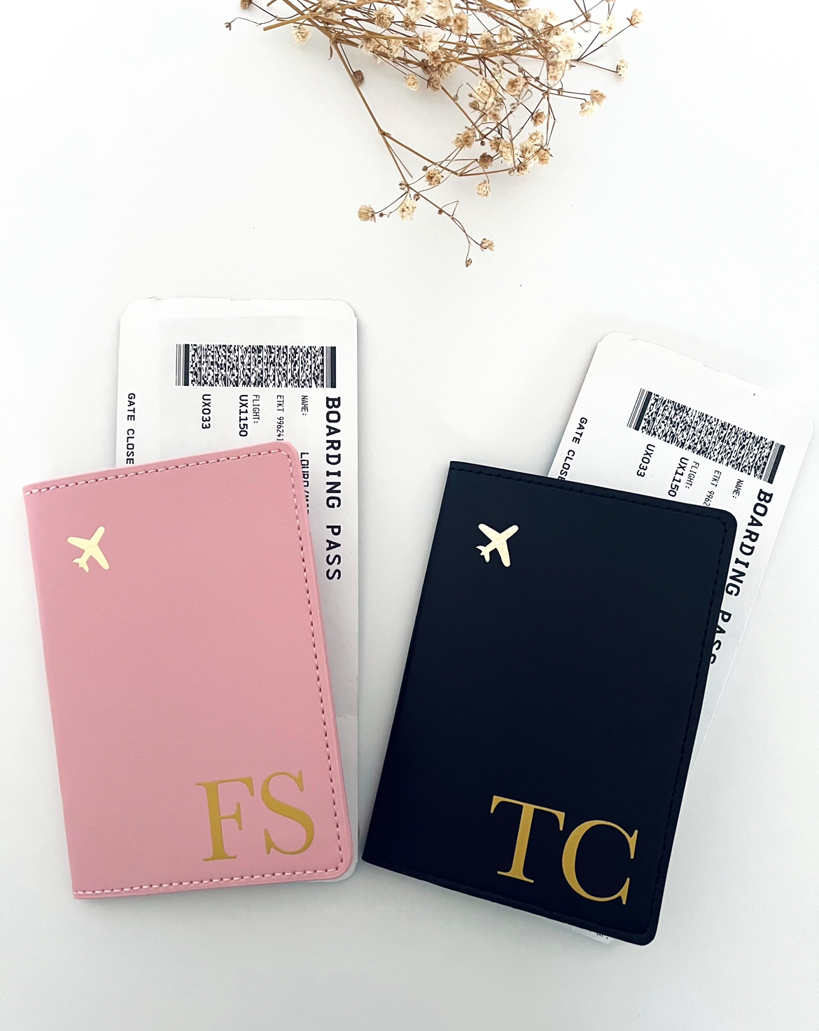 Capa de Passaporte Dois porta-cartões de embarque em couro sintético rosa e azul escuro com letras douradas FS e TC e ícone de avião, com cartões de embarque, sobre fundo branco e ramo seco.
