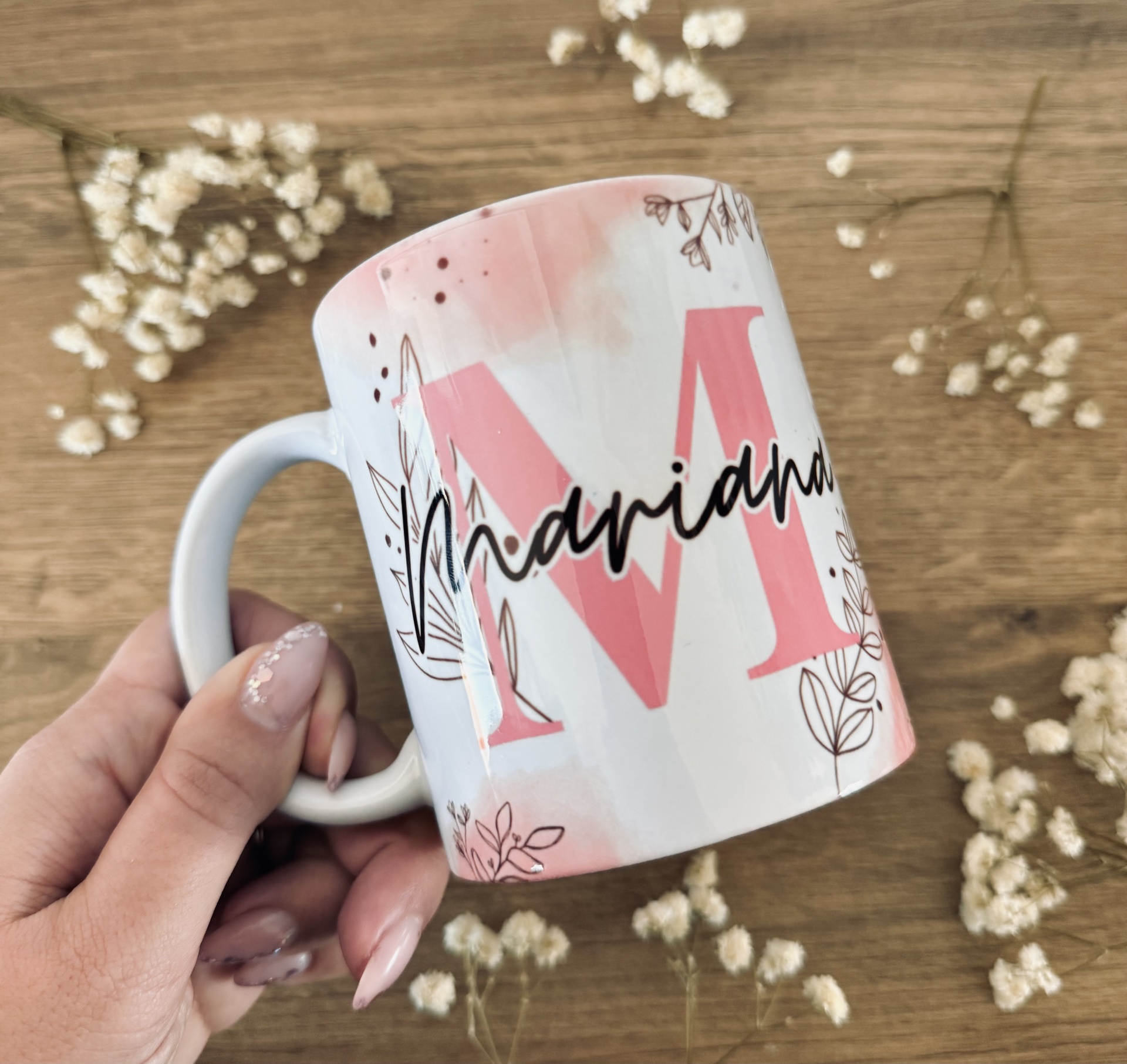 Caneca Flowers Caneca branca com letra M rosa, nome Mariana em preto e decoração floral sobre madeira com flores secas