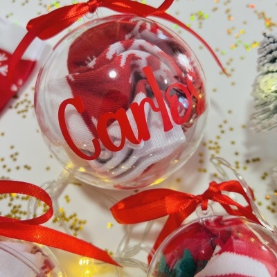 Bola de Natal transparente com meias vermelhas e brancas e nome 'Carlos'
