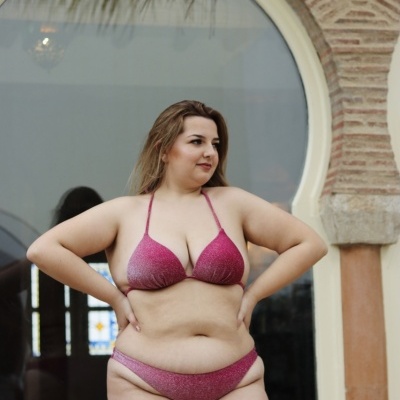 Mulher com biquíni rosa brilhante em frente a arco de tijolos