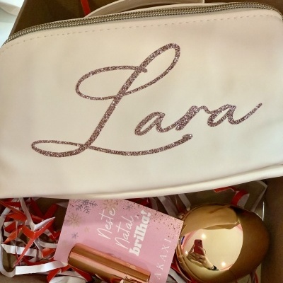 Mala de mão branca com texto glitter rosa e acessórios dourados dentro de caixa