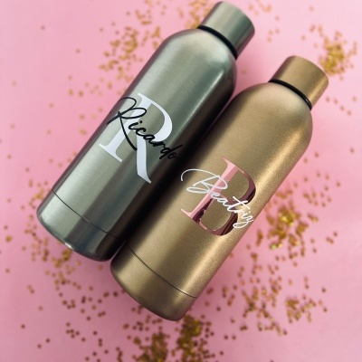 Garrafas metálicas personalizadas com nomes Ricardo e Betty em fundo rosa com confetes dourados