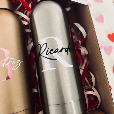 Frascos metálicos personalizados com nomes Ricardo e Beatriz dentro de uma caixa de presente com papel de enchimento e cartão 'I ♥ you'