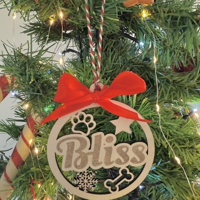 Enfeite de Natal em madeira com a palavra Bliss e elementos decorativos pendurado em árvore verde com luzes