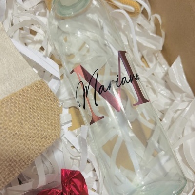 Garrafa de vidro personalizada numa caixa com enchimento branco e pequenos objetos de tecido e papel