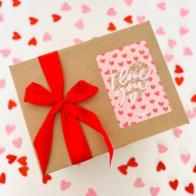 Caixa de presente com fita vermelha e cartão decorativo corações e texto 'I love you'
