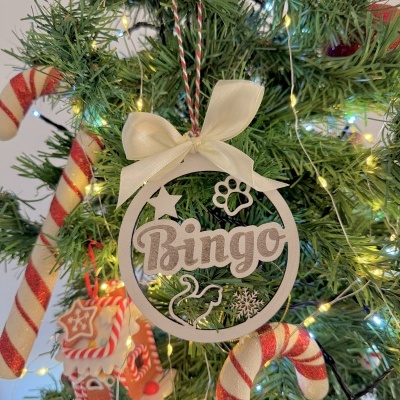 Ornamento de Natal de madeira com o nome Bingo pendurado numa árvore com luzes e decorações