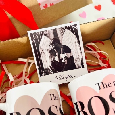 Duas canecas brancas com corações e texto, fotografia preto e branco de casal e cartão com corações em caixa de cartão