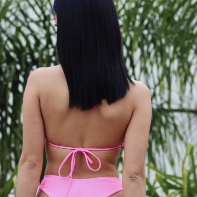 Mulher de costas com biquíni rosa fluorescente e plantas verdes ao fundo