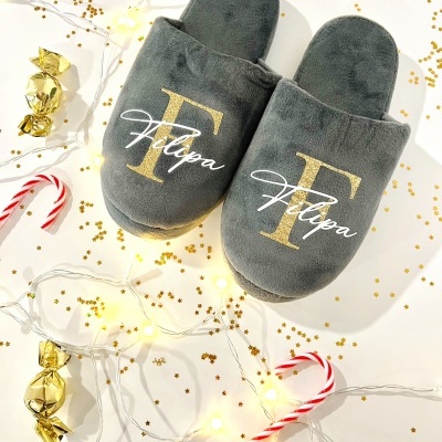 Chinelos cinzentos felpudos com letra F dourada e palavra Felipa em branco, com decoração de Natal ao redor