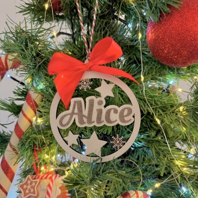 Decoração de Natal branca com nome Alice e laço vermelho numa árvore de Natal verde com luzes e ornamentos