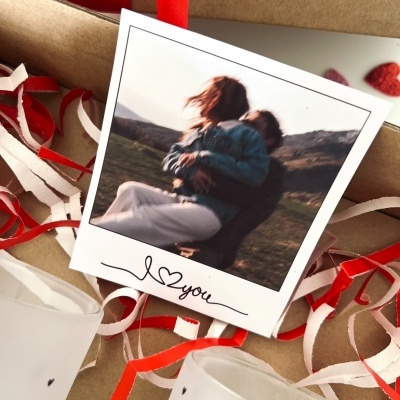 Fotografia polaroid de casal com fita vermelha e copos de vidro em fundo castanho