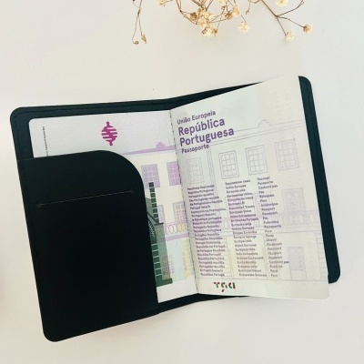 Capa preta de couro com passaporte português aberto e flores secas ao fundo