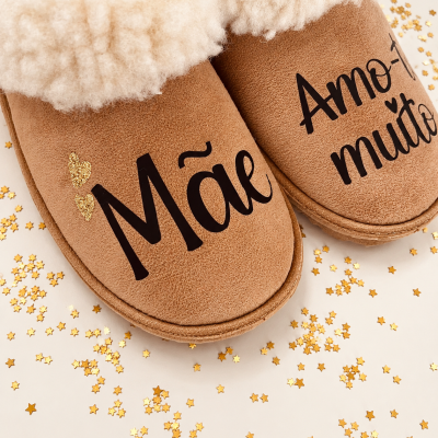 Pantufas castanhas com interior peludo branco e texto Mãe Amo-te muito sobre superfície com confetes dourados.