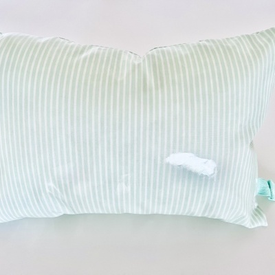 Travesseiro retangular riscado verde e branco com rasgão e etiquetas.