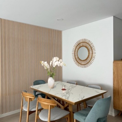 Mesa de jantar com tampo em pedra branca e cadeiras de madeira com estofado cinza e azul, com espelho redondo na parede