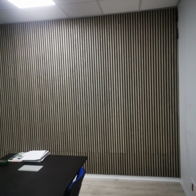 Parede de painéis verticais em madeira com mesa preta, cadeiras azuis e teto branco com luz.