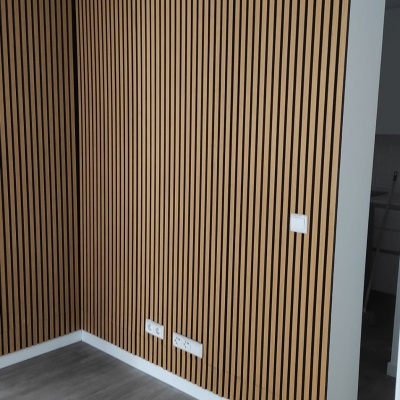 Parede com painéis de madeira ripados castanho claro com espaçamento preto e chão cinza claro