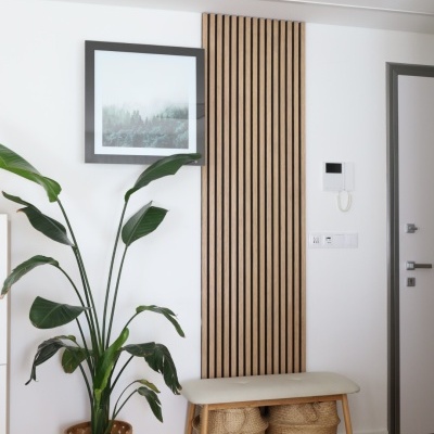 Banco em madeira clara com cestas de vime, planta grande em vaso de vime, painel de madeira e quadro na parede branca