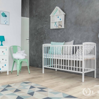 Quarto de bebé com berço branco, cómoda com padrão de gotas, cadeira verde-água e tapete geométrico