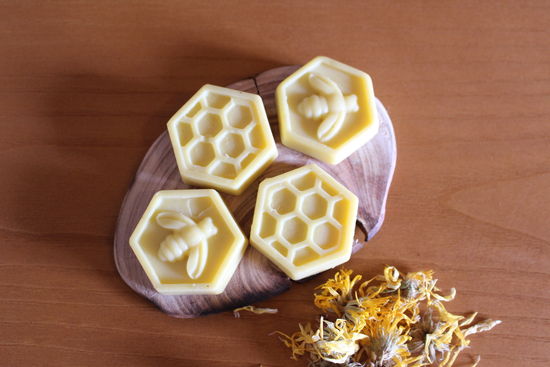 Sabonetes amarelos em formato hexagonal com padrões de colmeia e abelha sobre tábua de madeira