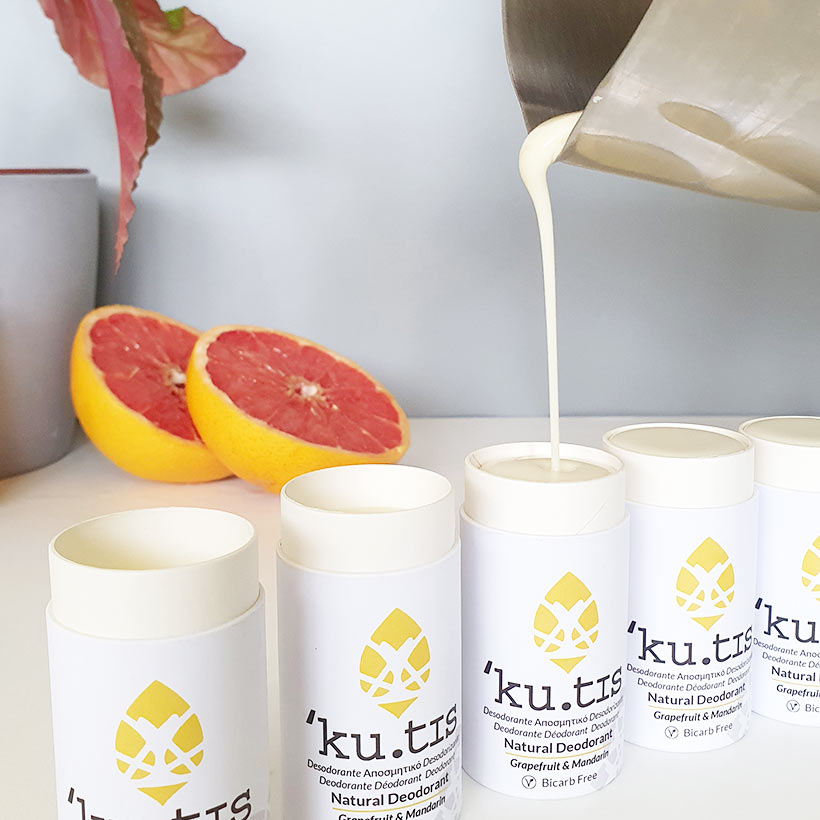 Desodorizante Natural Vegano Kutis – Sem Bicarbonato Desodorizantes naturais 'ku.tis' em embalagens brancas com detalhes amarelos, meio toranja e jarro a verter líquido cremoso