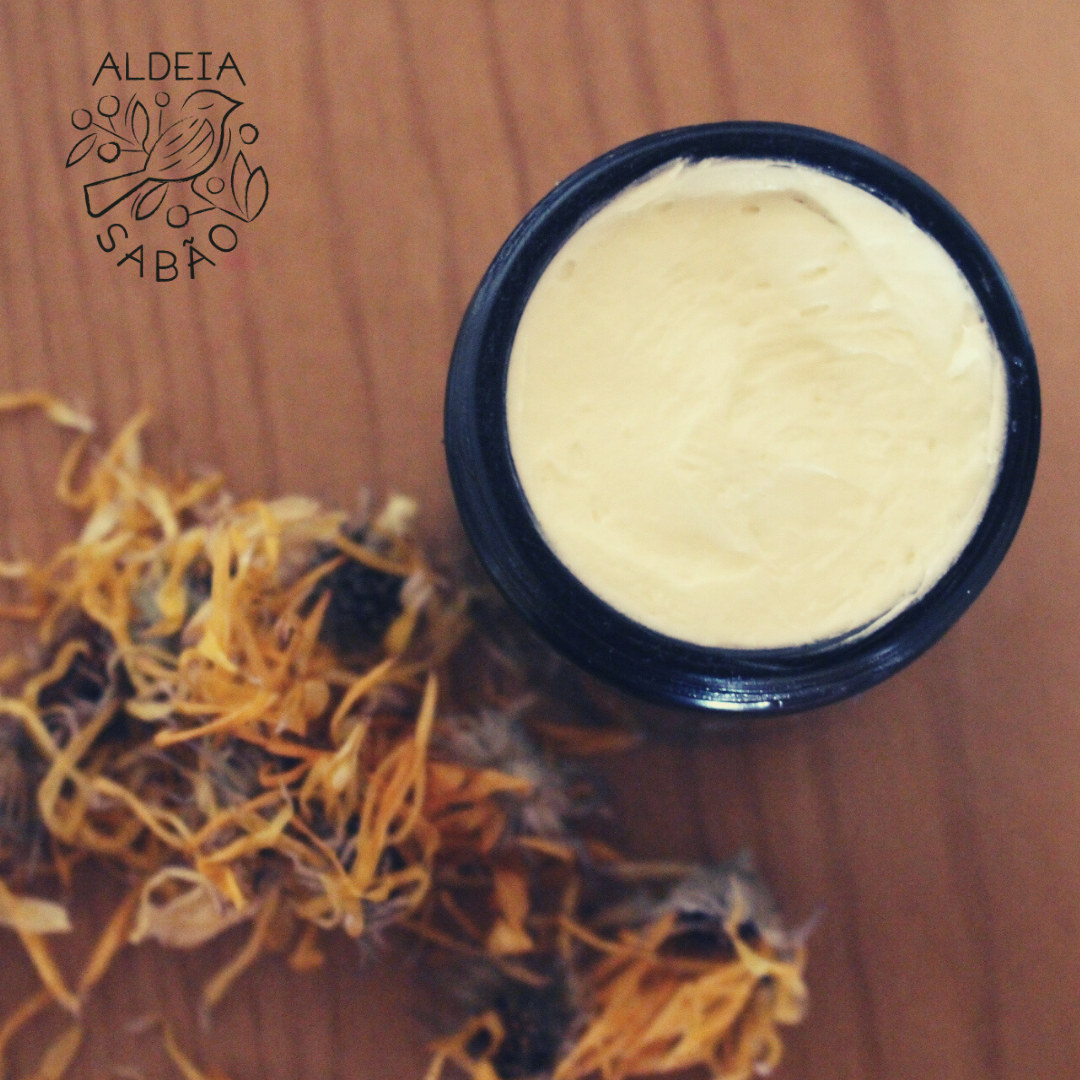 Receita de Manteiga Corporal Calêndula & Karité Frasco preto com creme amarelo e flores secas ao lado, sobre fundo de madeira