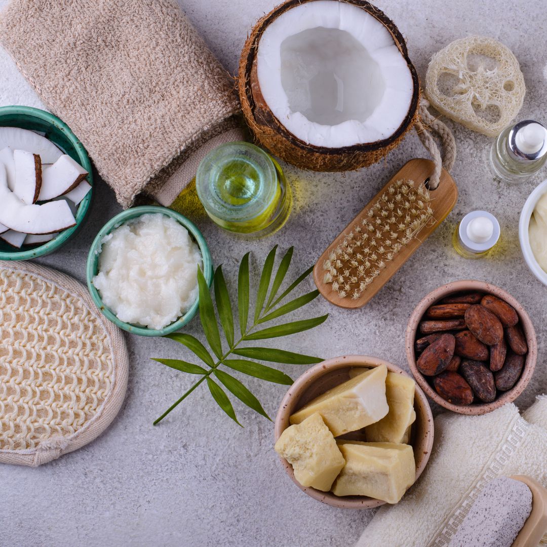 Produtos naturais de cuidado corporal, óleo, manteiga, coco, escova de massagem e esponjas sobre superfície cinza