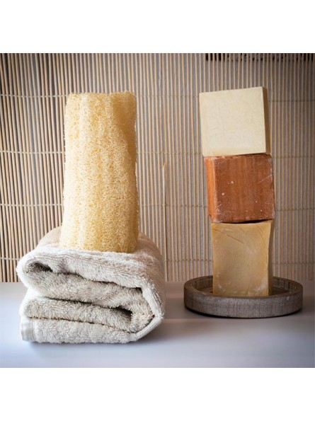 Esponja de luffa Azal Esponja natural amarela sobre toalha bege e três barras de sabão empilhadas em prato de madeira