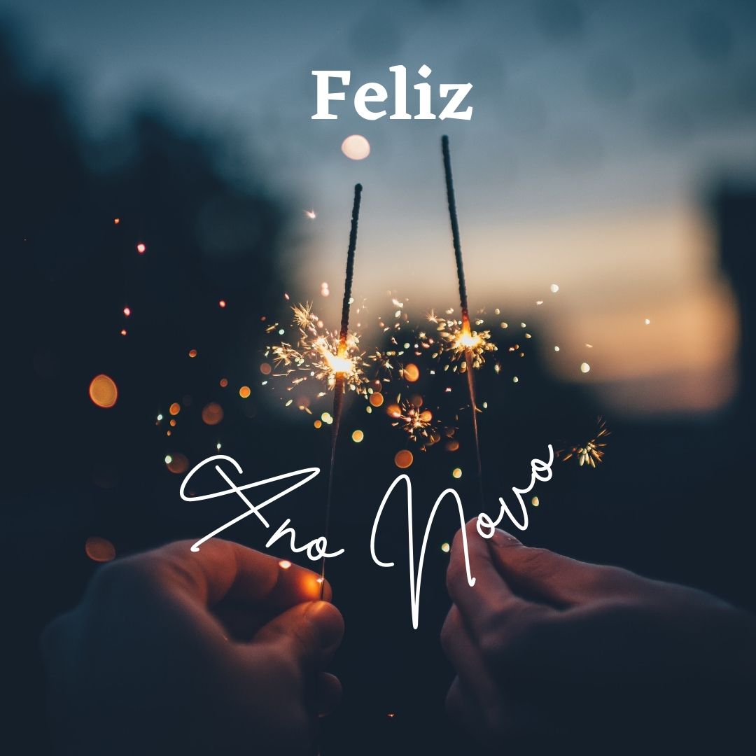 Novo Ano, Novos Hábitos Duas mãos segurando fogo-de-artifício aceso ao anoitecer com texto Feliz Ano Novo