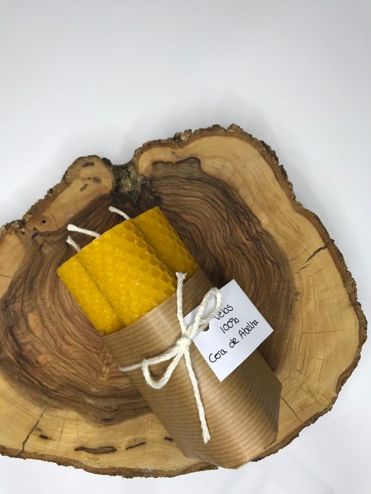 Velas de cera de abelha (conjunto 3) Vela amarela de cera de abelha enrolada em papel castanho com etiqueta e laço, sobre pedaço de madeira rústica.