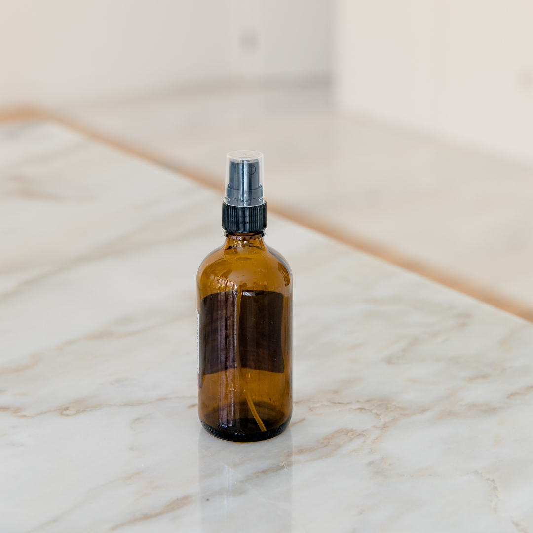 Garrafa de vidro âmbar com spray (100 ml) Frasco de vidro âmbar com tampa de spray preta sobre superfície de mármore branco