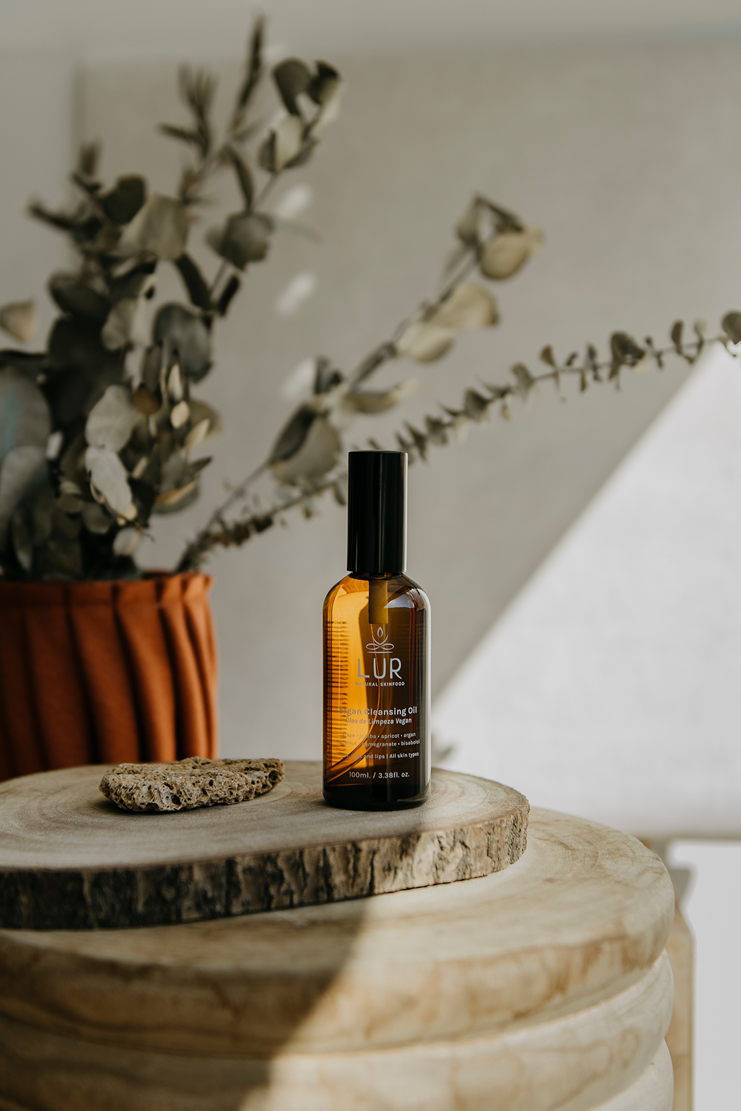 Óleo de limpeza LUR Frasco âmbar de óleo facial ULUR sobre mesa de madeira com vaso e folhas secas ao fundo