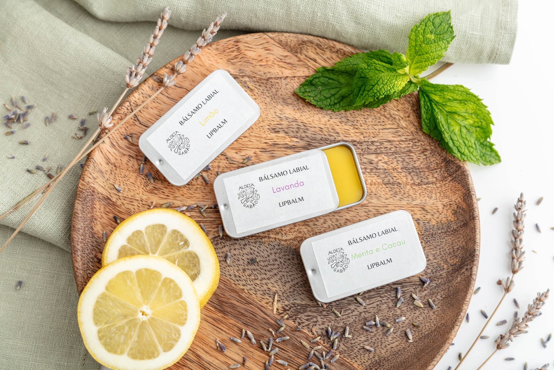 Três latas pequenas de velas perfumadas em base de madeira com limões e folhas verdes