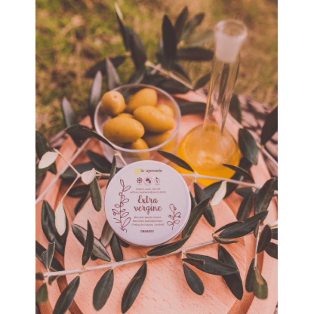 Creme de mãos com Azeite Extra Virgem Creme Extra Vergine da la saponaria, azeitonas verdes e frasco de líquido amarelo sobre tábua de madeira com folhas verdes