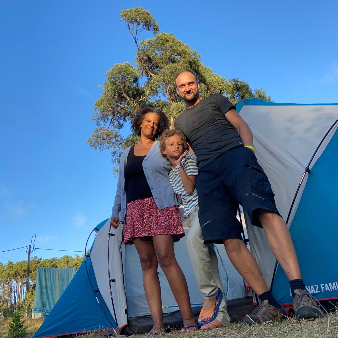 Família em frente a tenda de campismo azul e branca ao ar livre com céu azul