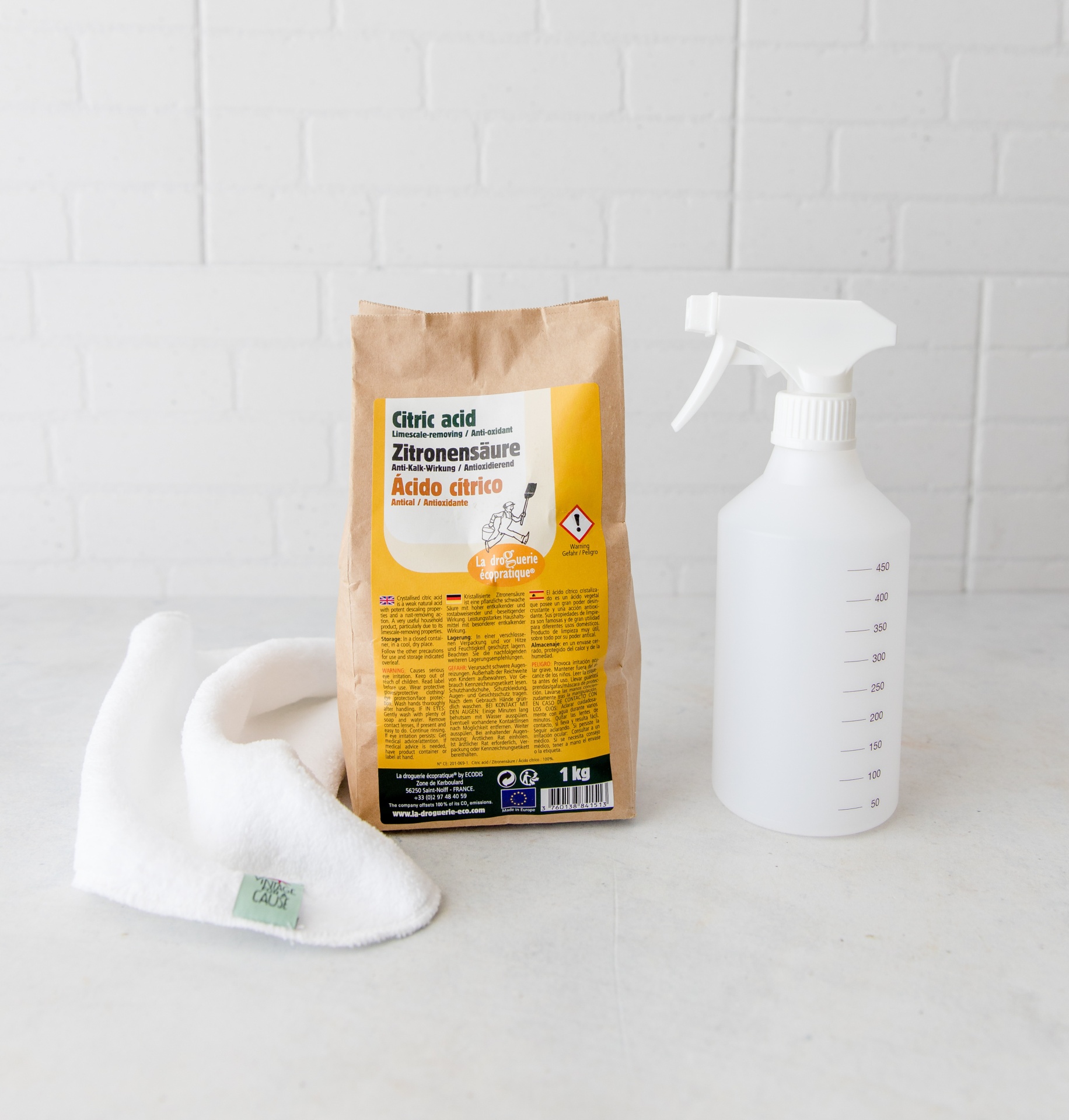 Pacote de ácido cítrico com rótulo amarelo, frasco spray plástico transparente e pano branco