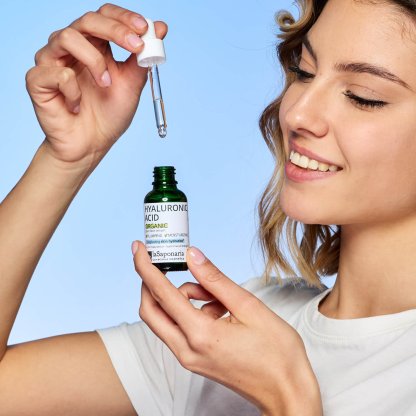 Ácido Hialurónico - La Saponaria Mulher segura frasco verde de ácido hialurónico com conta-gotas branco e fundo azul