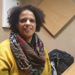 Mulher com cachecol colorido e casaco amarelo sentada em ambiente interior