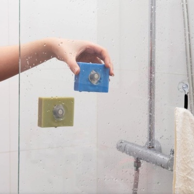 Esponjas quadradas azul e verde-oliva com ventosas transparentes numa cabine de duche