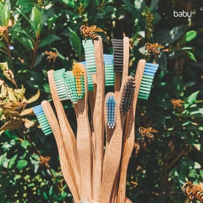 Escovas de dentes de madeira com cerdas coloridas e abelhas voando num fundo natural